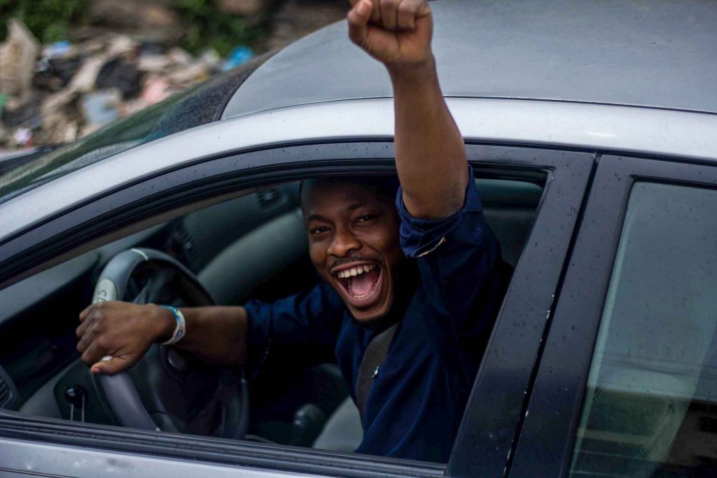 A man smiling and pumping his fist while driving a car