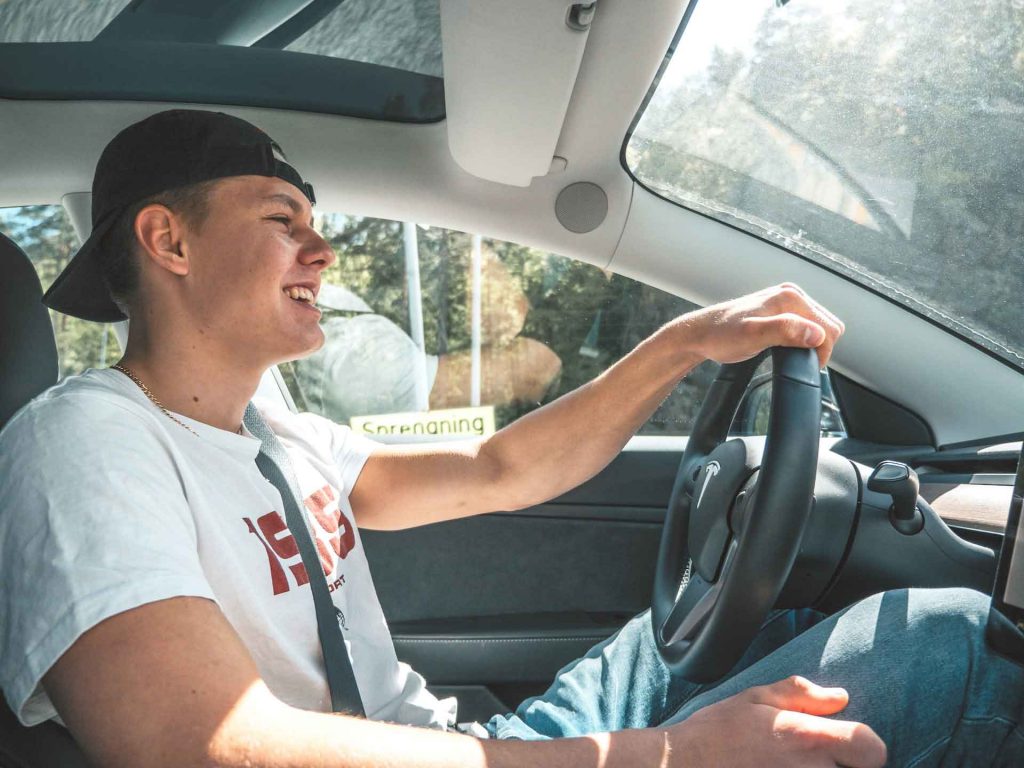 A young man smiling at the wheel of a car